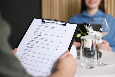 Photo of Couple choosing dishes from menu at table in restaurant, closeup