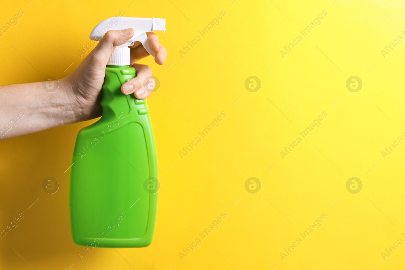 Photo of Woman with spray bottle of cleaning product on yellow background, closeup. Space for text