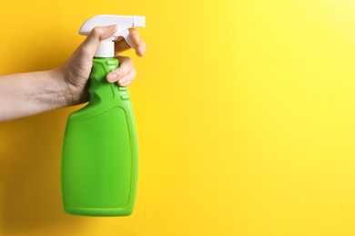 Photo of Woman with spray bottle of cleaning product on yellow background, closeup. Space for text