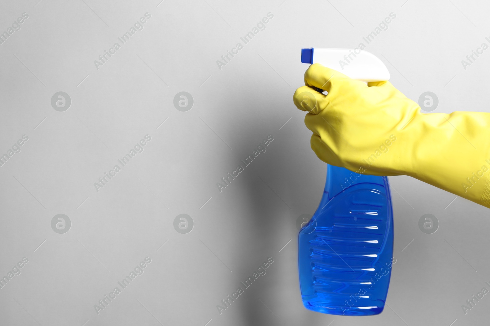 Photo of Woman with spray bottle of cleaning product on light grey background, closeup. Space for text