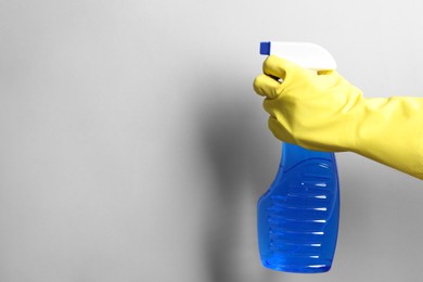 Photo of Woman with spray bottle of cleaning product on light grey background, closeup. Space for text