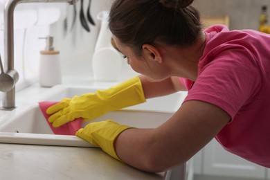 Photo of Woman cleaning sink with rag in kitchen