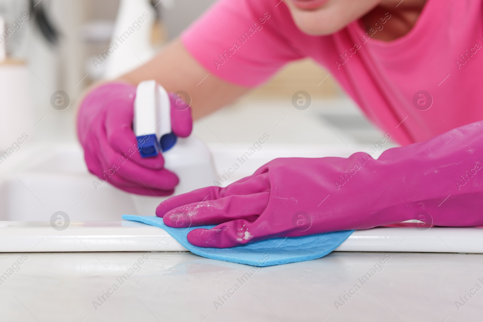 Photo of Woman using cleaning product while wiping sink with rag in kitchen, closeup