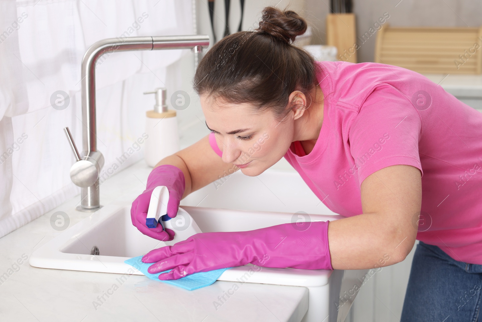 Photo of Woman using cleaning product while wiping sink with rag in kitchen