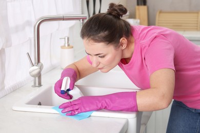 Photo of Woman using cleaning product while wiping sink with rag in kitchen