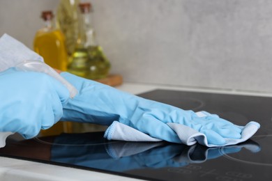 Photo of Woman using cleaning product while wiping induction cooktop with rag in kitchen, closeup