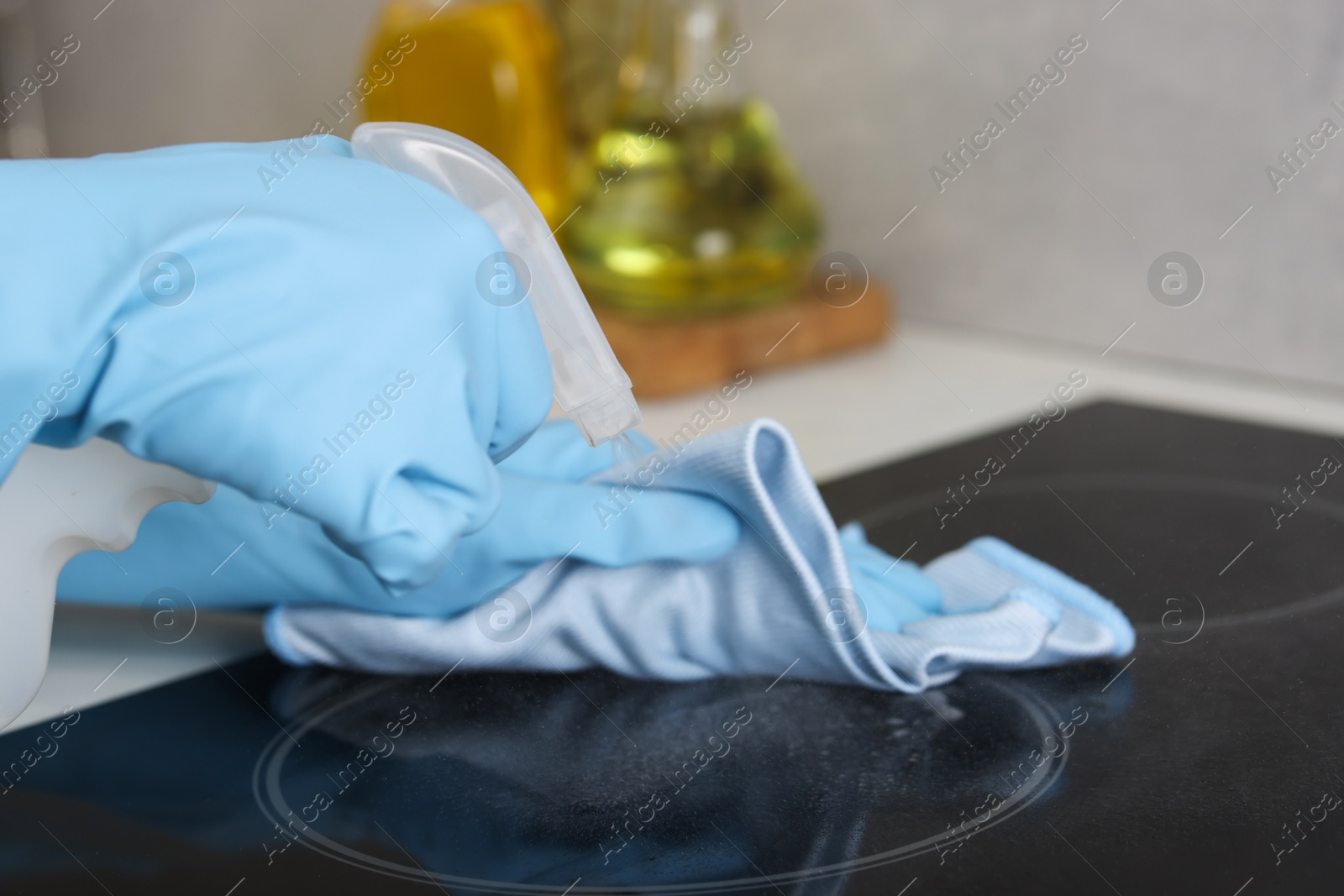 Photo of Woman using cleaning product while wiping induction cooktop with rag in kitchen, closeup. Space for text