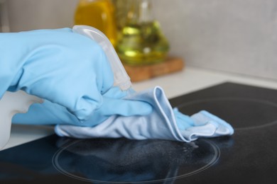 Photo of Woman using cleaning product while wiping induction cooktop with rag in kitchen, closeup. Space for text