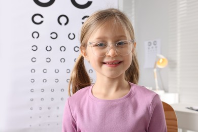 Photo of Little girl trying glasses against vision test chart