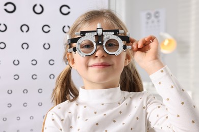 Photo of Little girl with trial frame against vision test chart. Eye examination