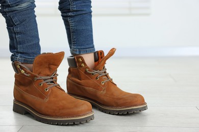 Photo of Child wearing oversized brown boots indoors, closeup. Space for text