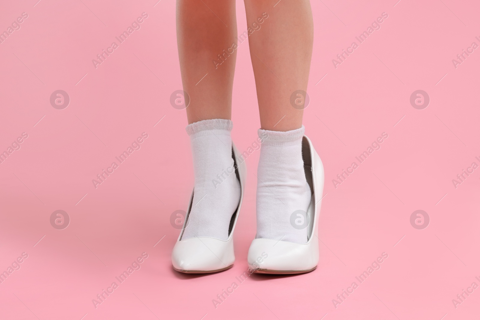 Photo of Little girl wearing oversized high heeled shoes on pink background, closeup