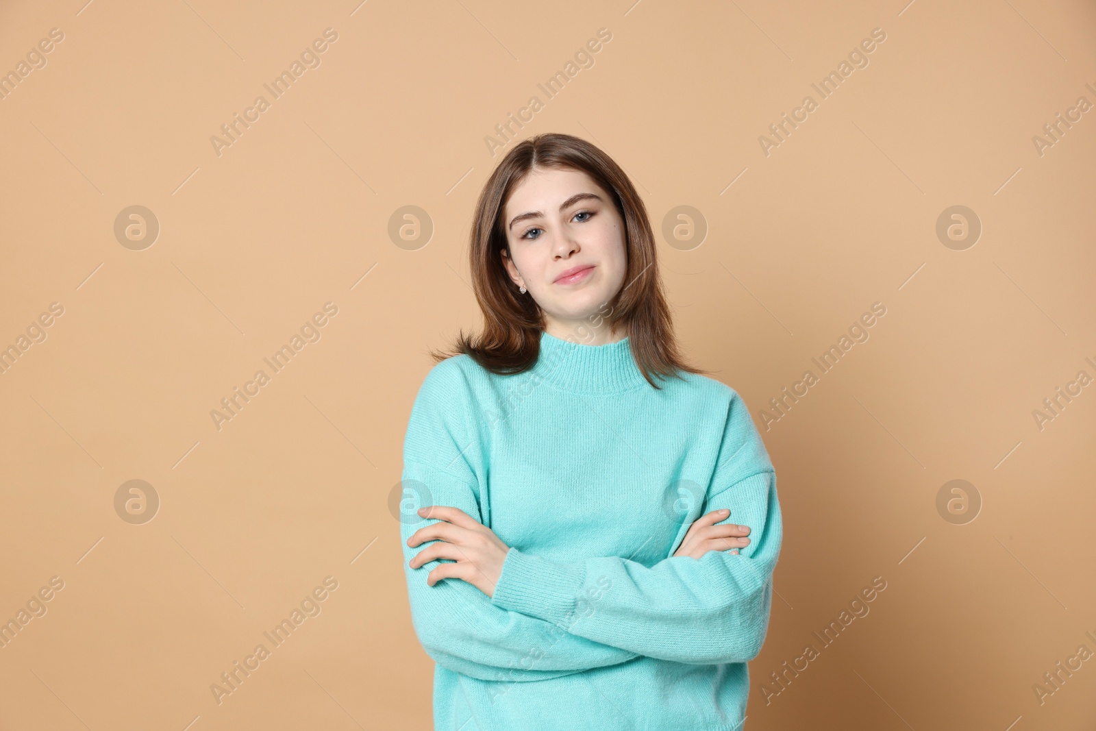 Photo of Portrait of beautiful teenage girl with crossed arms on beige background