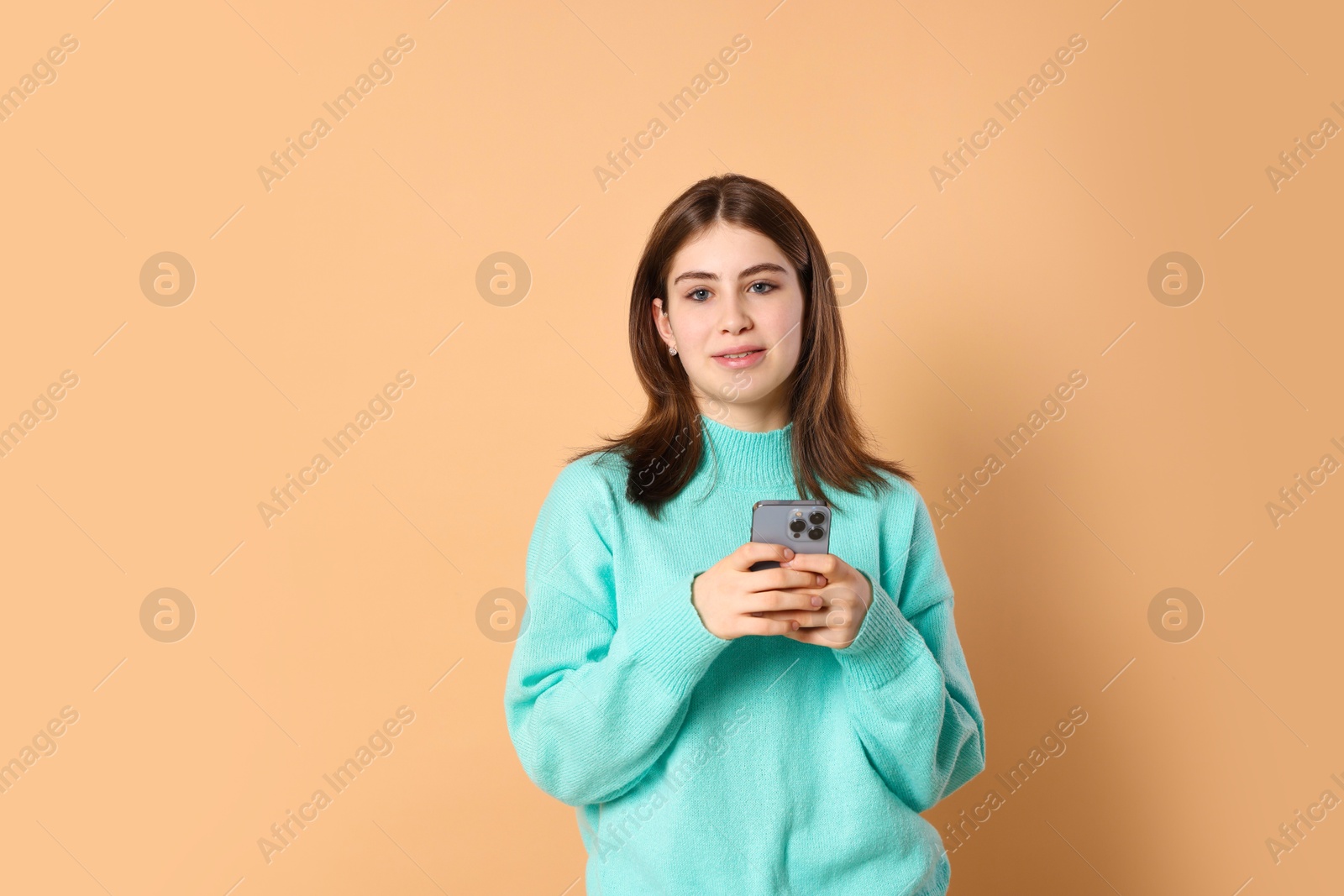 Photo of Portrait of beautiful teenage girl with smartphone on beige background. Space for text