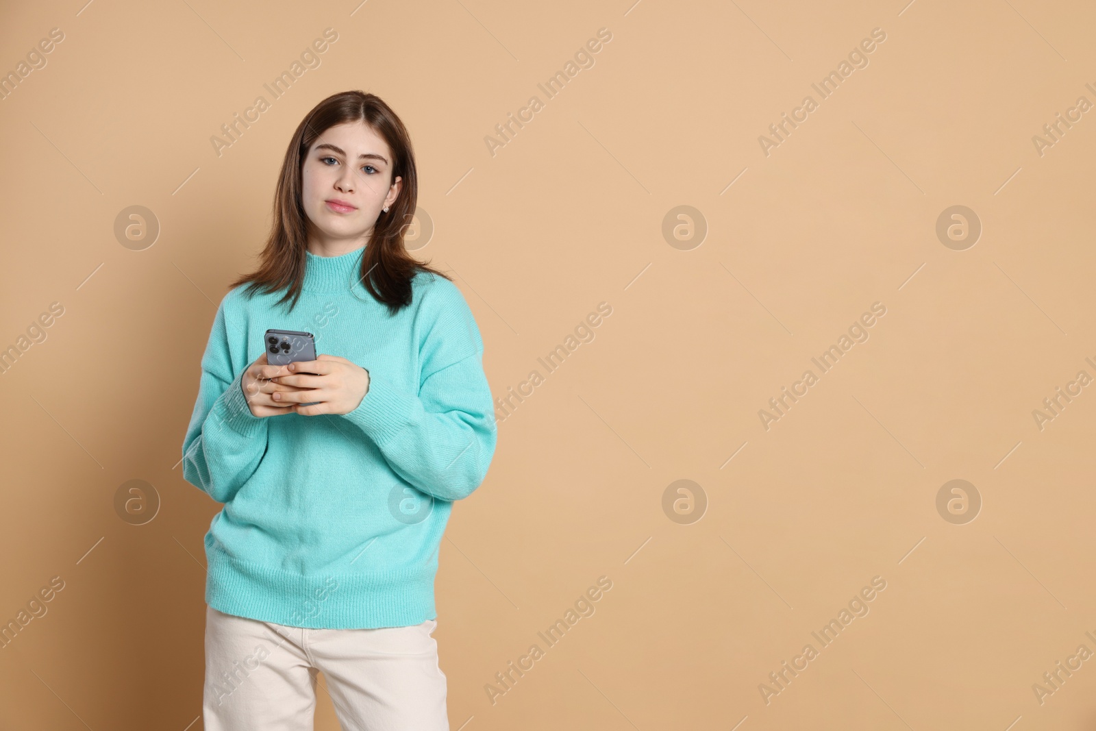 Photo of Portrait of beautiful teenage girl with smartphone on beige background. Space for text