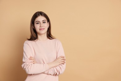 Photo of Portrait of beautiful teenage girl with crossed arms on beige background. Space for text