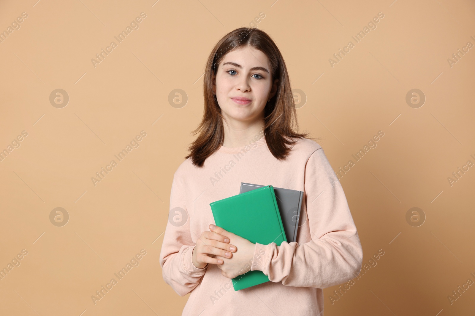 Photo of Portrait of teenage girl with books on beige background