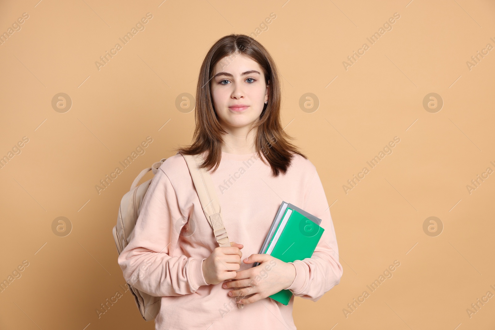 Photo of Portrait of teenage girl with books and backpack on beige background