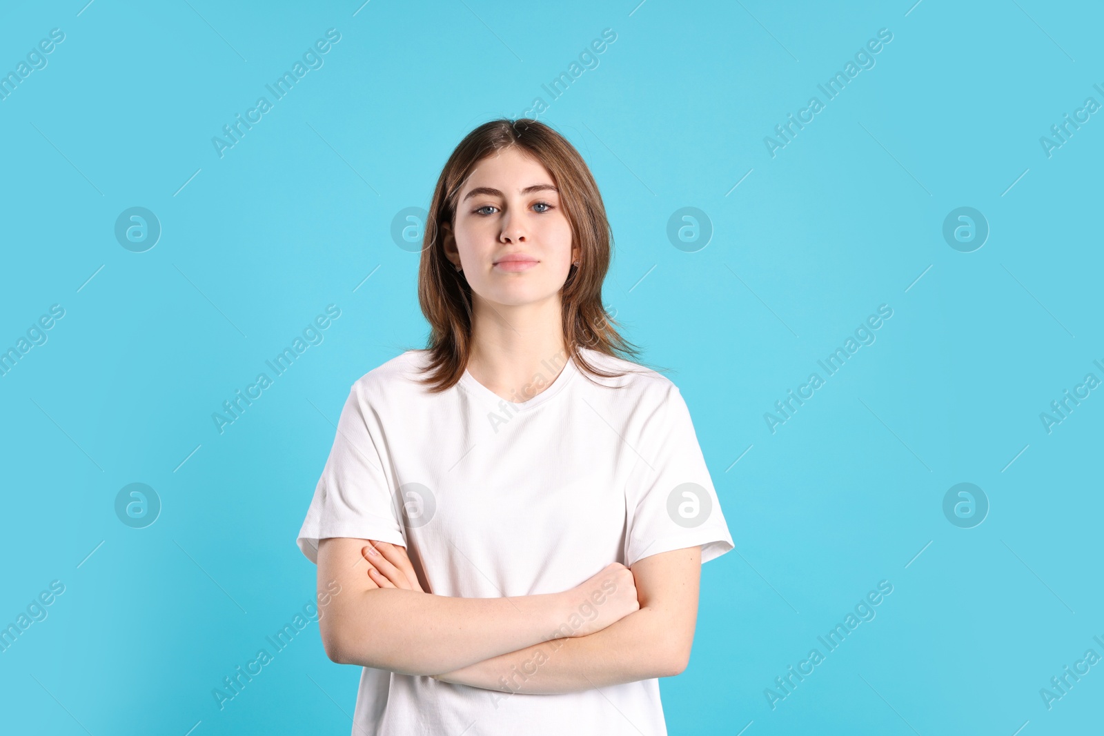 Photo of Portrait of beautiful teenage girl with crossed arms on light blue background