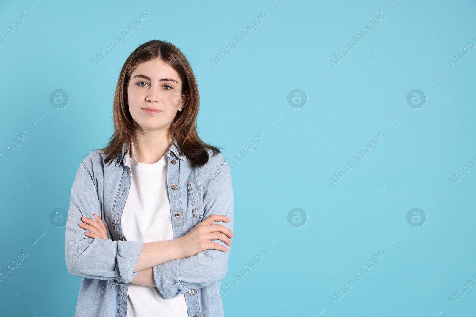 Photo of Portrait of beautiful teenage girl with crossed arms on light blue background. Space for text