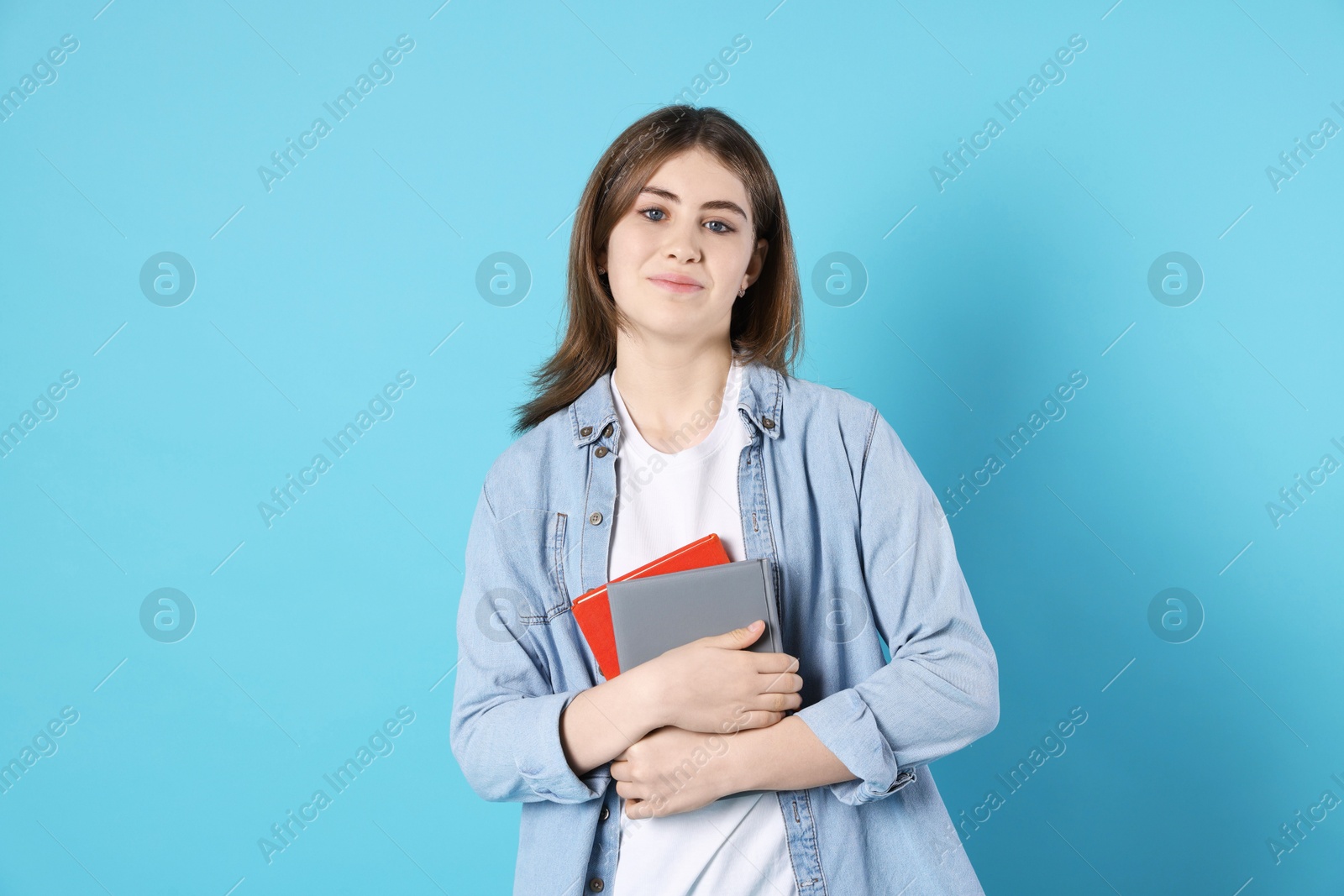 Photo of Portrait of teenage girl with books on light blue background