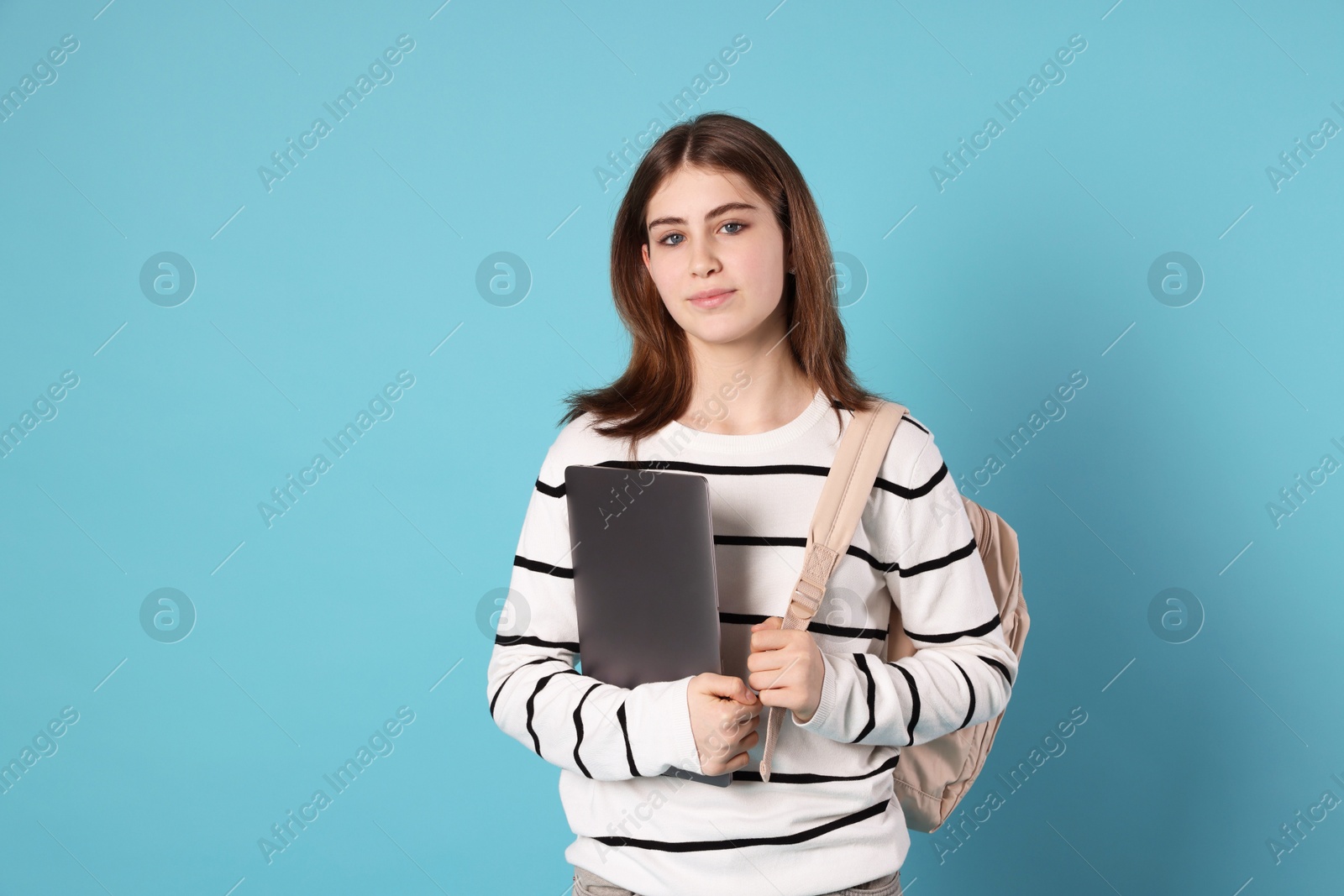 Photo of Portrait of teenage girl with laptop and backpack on light blue background