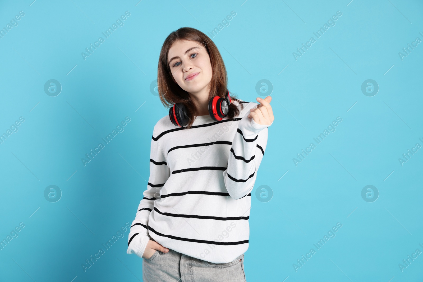 Photo of Portrait of teenage girl with headphones showing mini heart gesture on light blue background