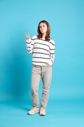 Photo of Teenage girl with headphones showing V-sign on light blue background