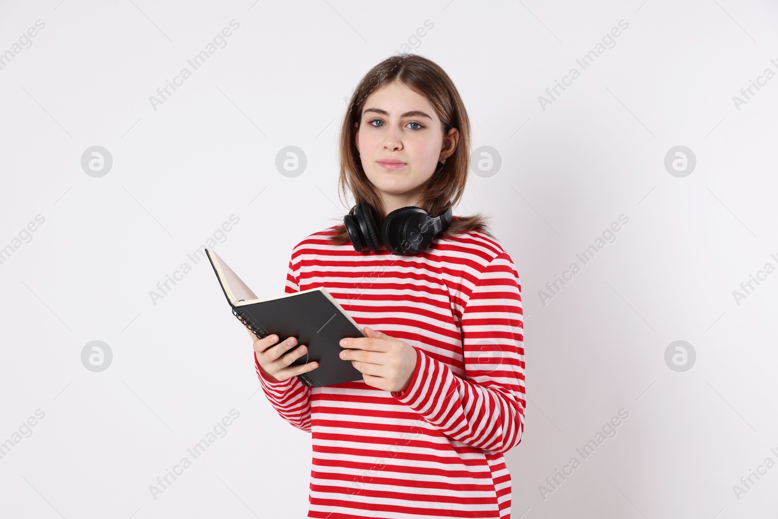 Photo of Portrait of teenage girl with headphones reading book on light background