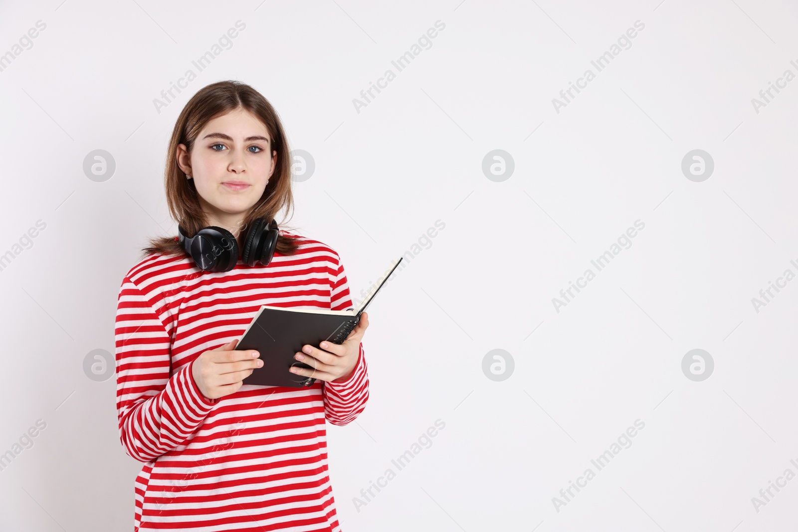 Photo of Portrait of teenage girl with headphones reading book on light background. Space for text