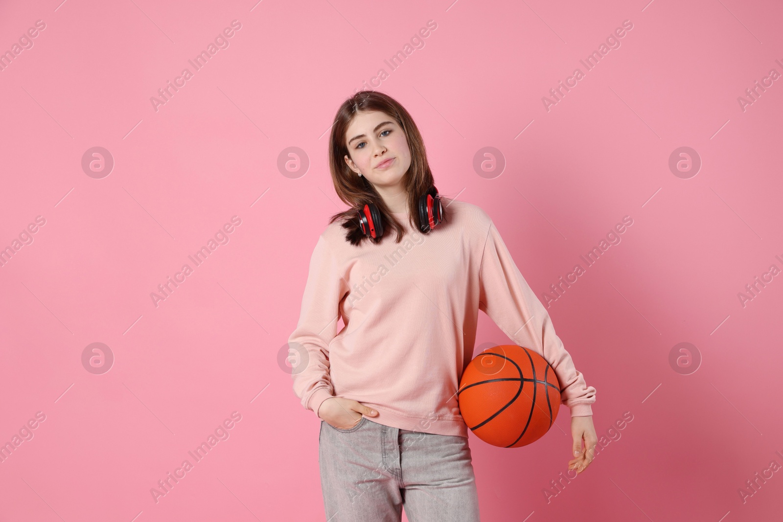 Photo of Portrait of teenage girl with headphones and basketball ball on pink background