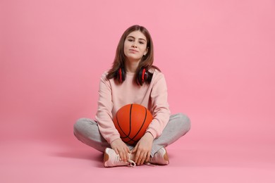 Photo of Beautiful teenage girl with headphones and basketball ball on pink background