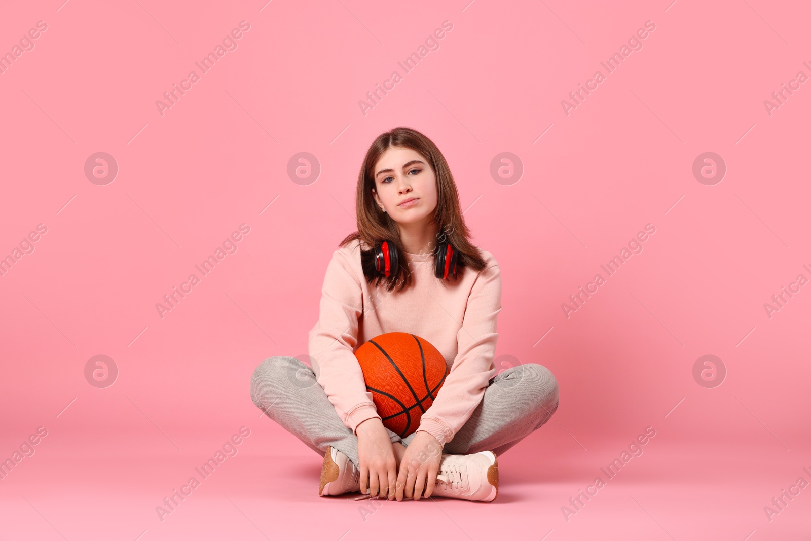 Photo of Beautiful teenage girl with headphones and basketball ball on pink background