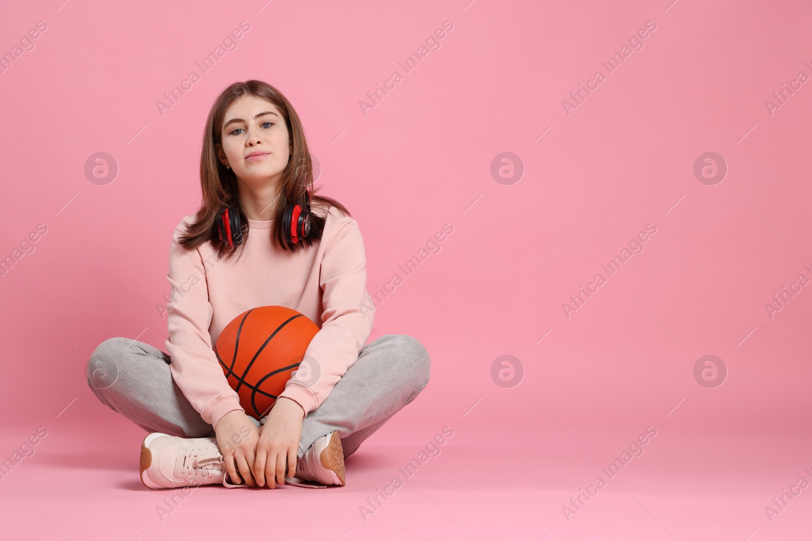 Photo of Beautiful teenage girl with headphones and basketball ball on pink background. Space for text