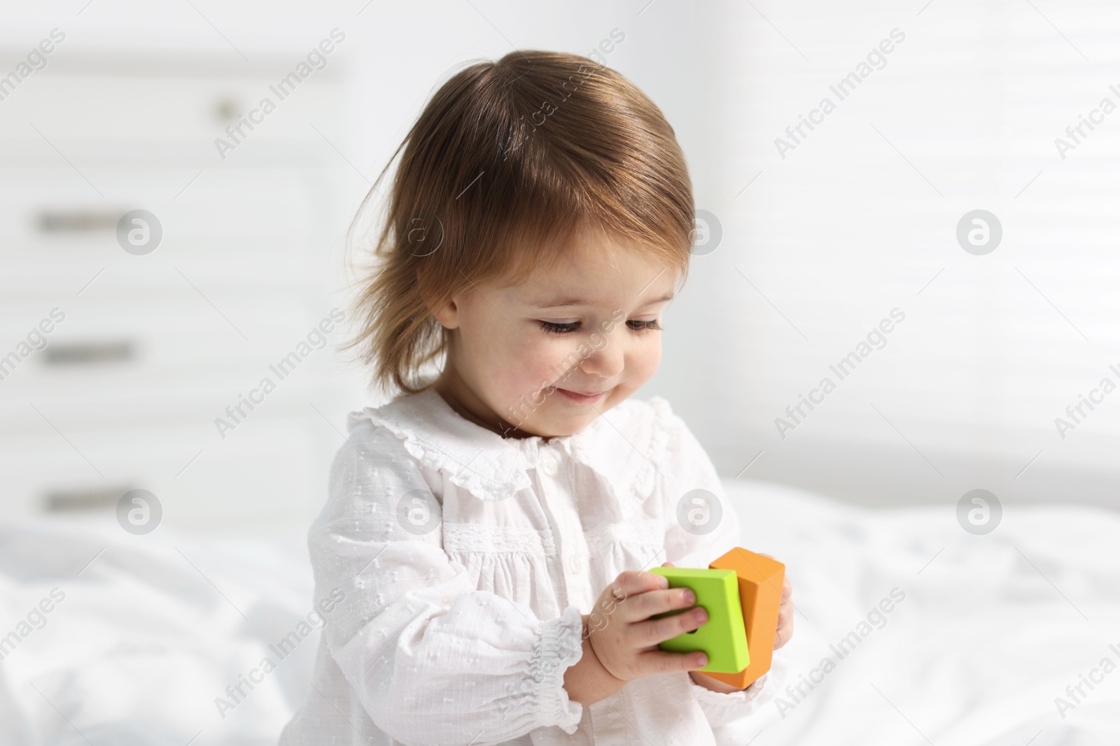 Photo of Cute little baby girl playing with toy on bed at home