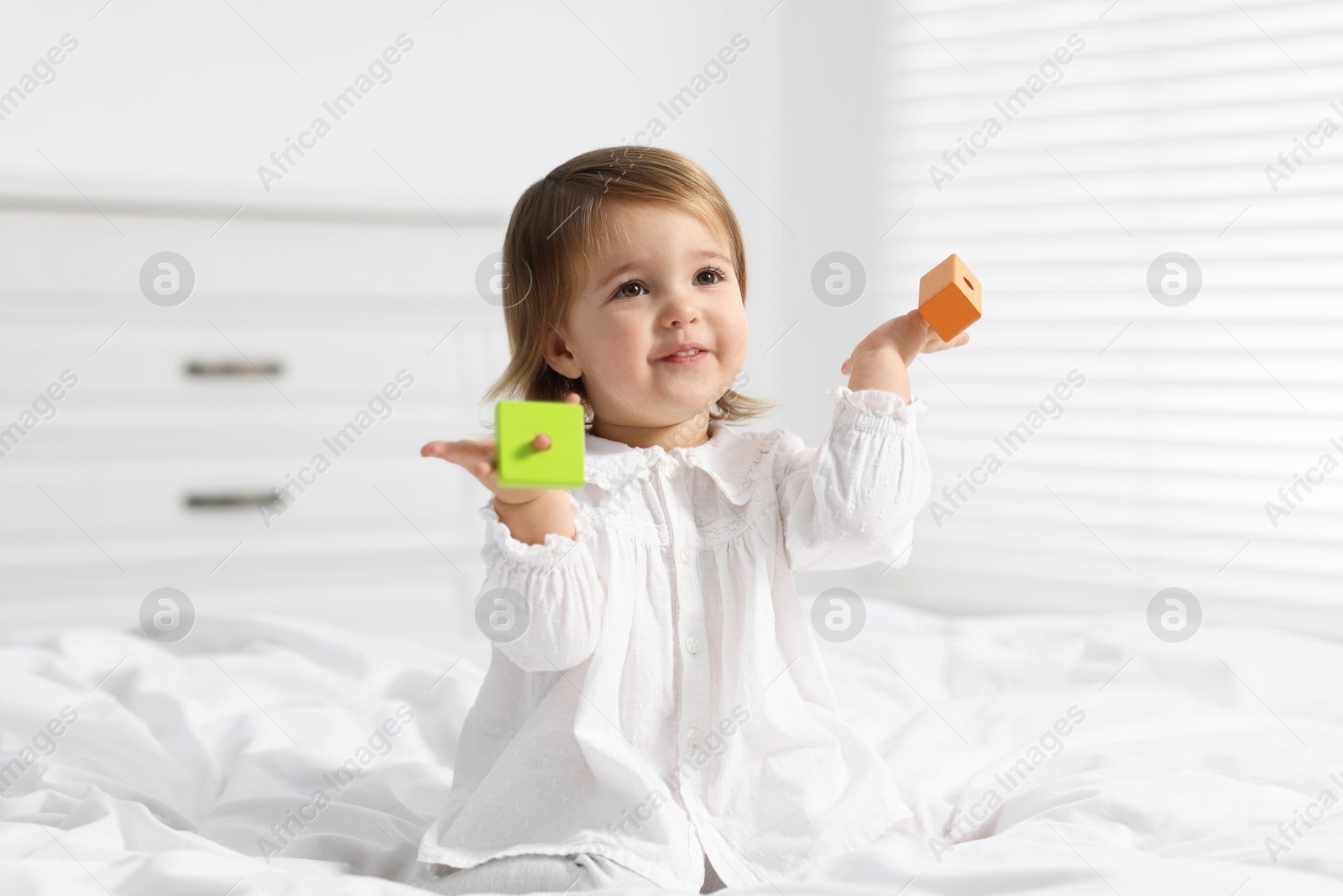 Photo of Cute little baby girl playing with toy on bed at home