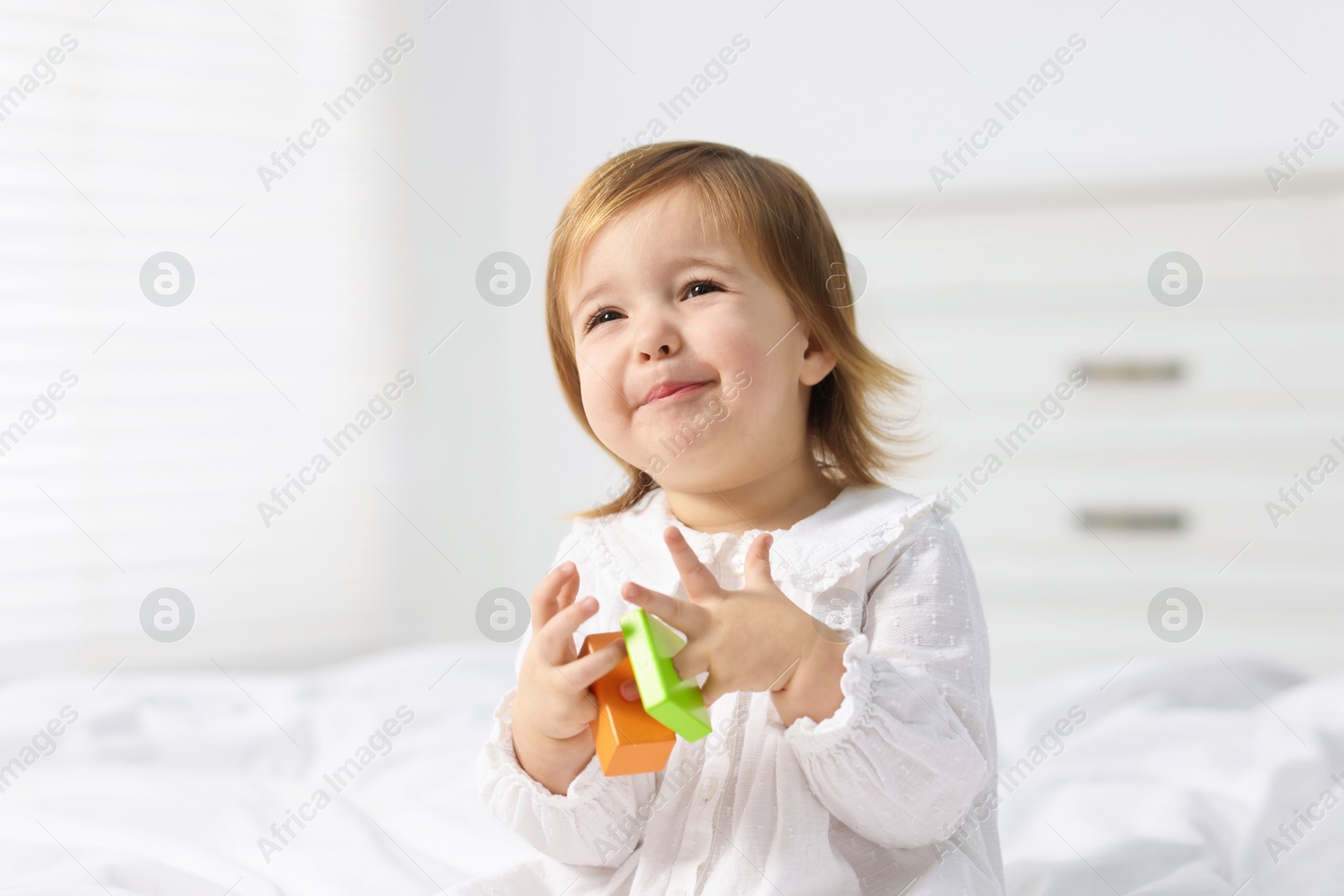 Photo of Cute little baby girl playing with toy on bed at home