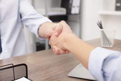 Photo of Businessmen shaking hands at wooden desk in office, closeup