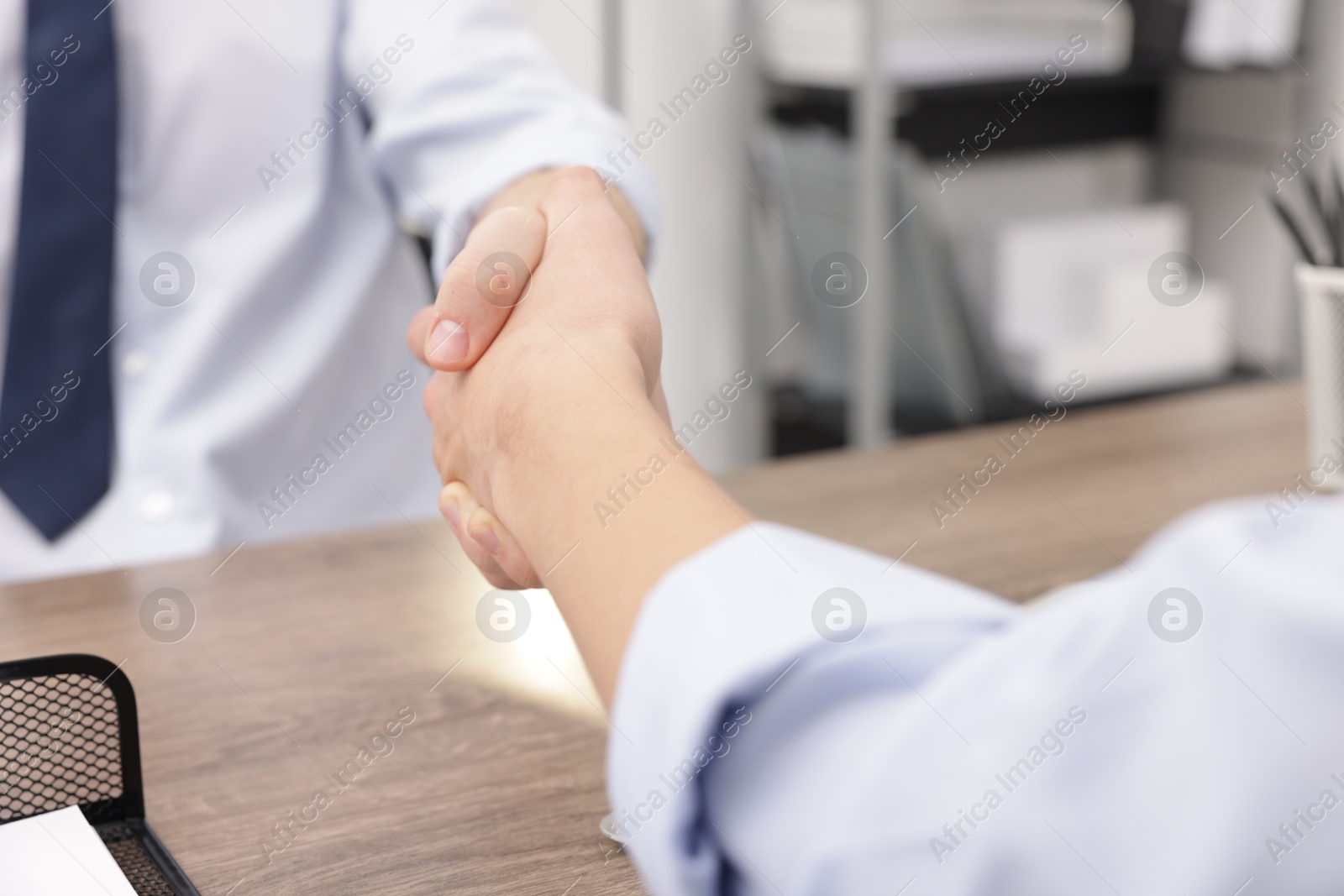 Photo of Businessmen shaking hands at wooden desk in office, closeup