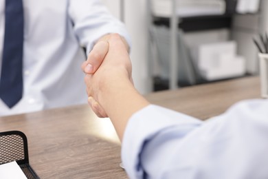 Businessmen shaking hands at wooden desk in office, closeup