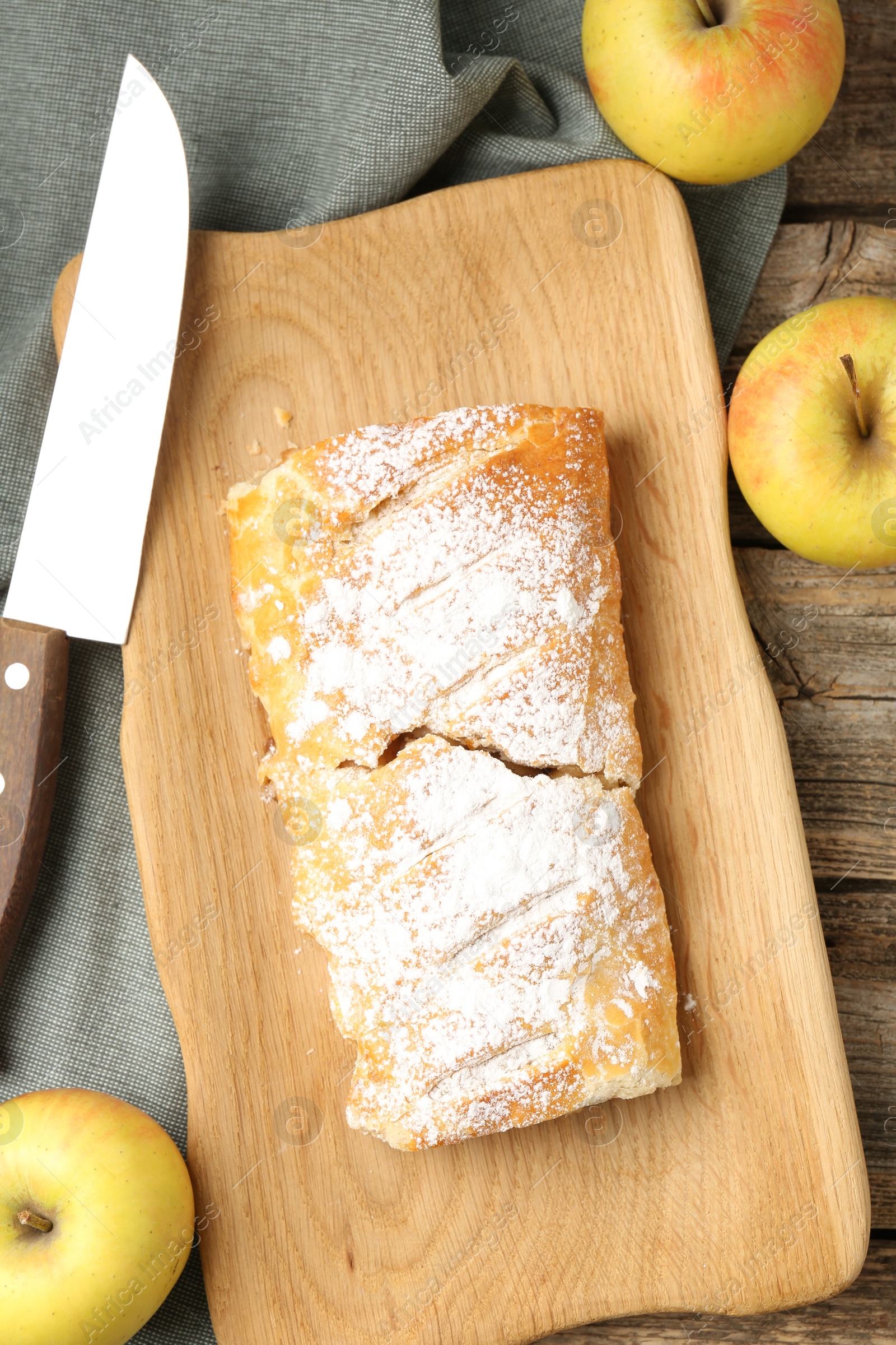 Photo of Delicious strudel with apples, powdered sugar and knife on wooden table, flat lay