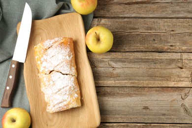 Delicious strudel with apples, powdered sugar and knife on wooden table, flat lay. Space for text