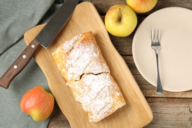 Photo of Delicious strudel with apples, powdered sugar and knife on wooden table, flat lay