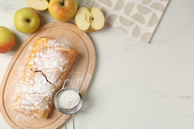 Photo of Delicious strudel with apples and powdered sugar on white marble table, flat lay. Space for text