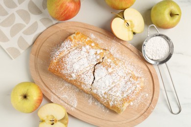 Delicious strudel with apples and powdered sugar on white marble table, flat lay