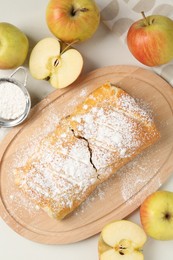 Delicious strudel with apples and powdered sugar on white table, flat lay