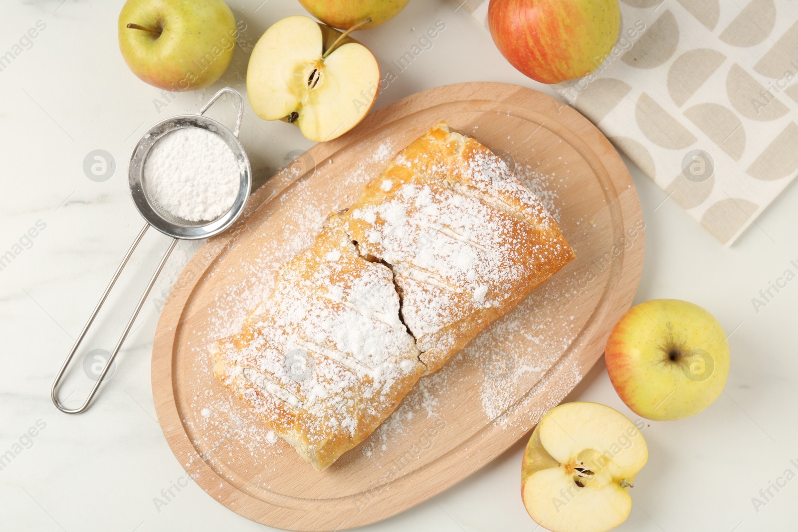 Photo of Delicious strudel with apples and powdered sugar on white marble table, flat lay