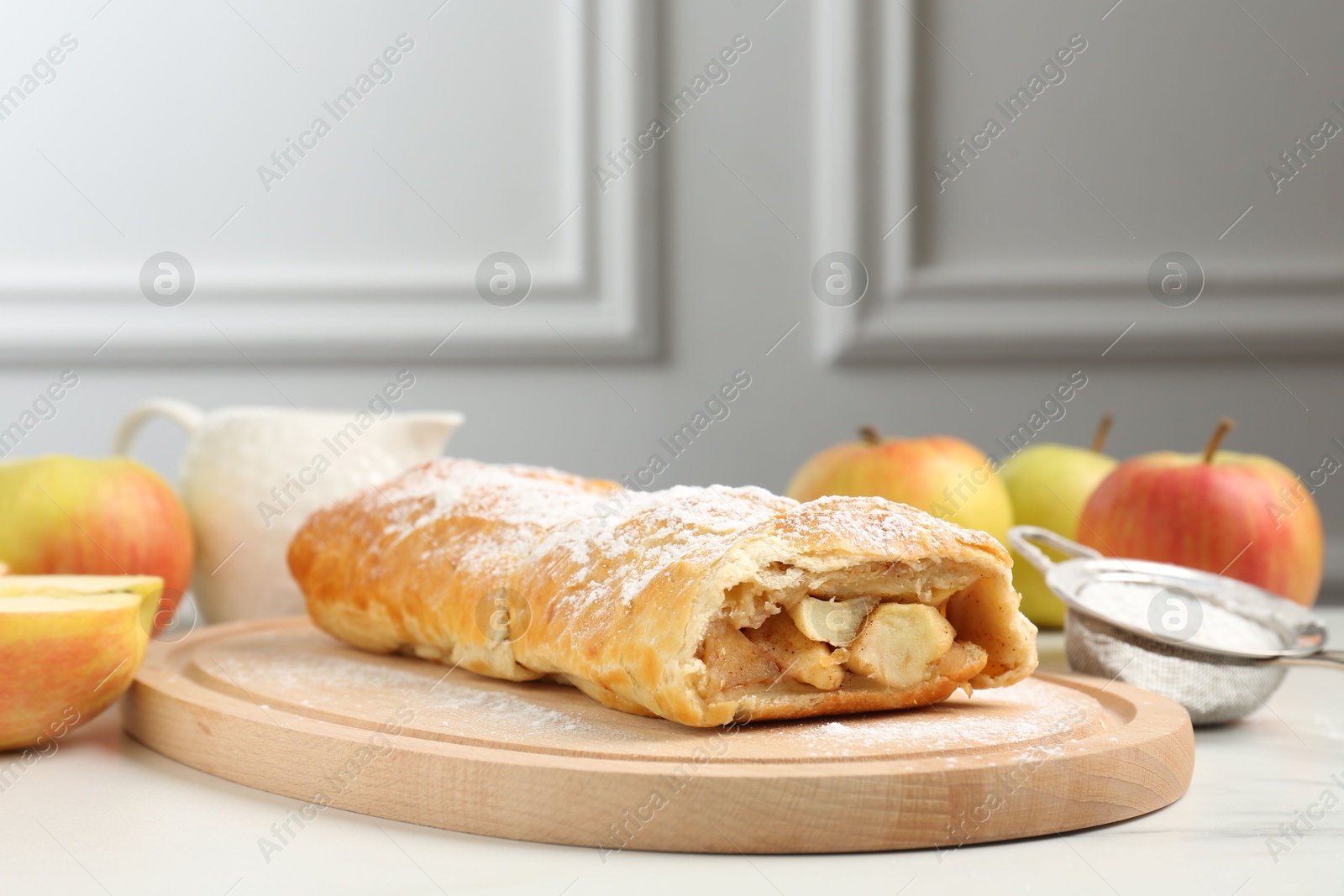 Photo of Delicious strudel with apples and powdered sugar on white marble table, closeup