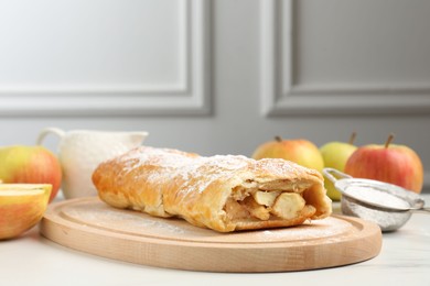 Delicious strudel with apples and powdered sugar on white marble table, closeup