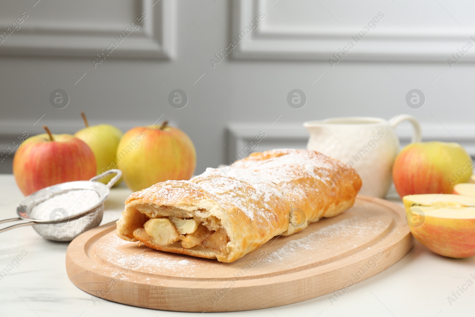 Photo of Delicious strudel with apples and powdered sugar on white marble table, closeup